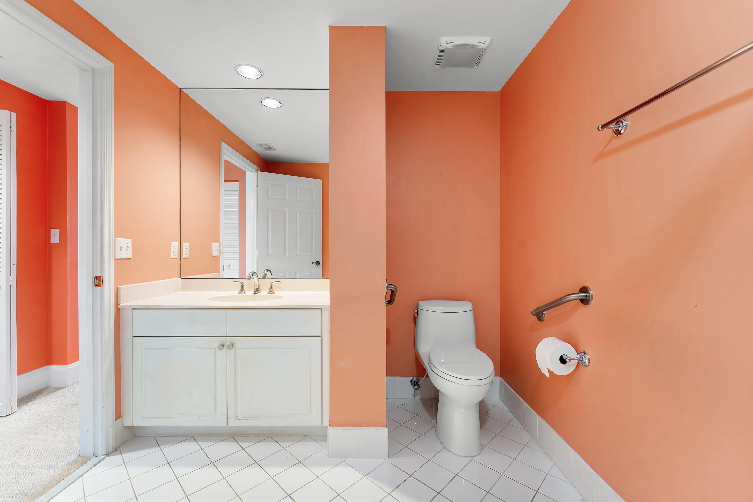 Bathroom featuring a white vanity with an integrated countertop, large wall mirror, and white tile flooring