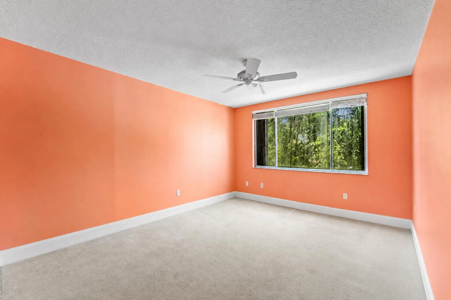 Spacious room featuring broad windows with blinds, a ceiling fan, light-toned carpeting, and a substantial baseboard trim
