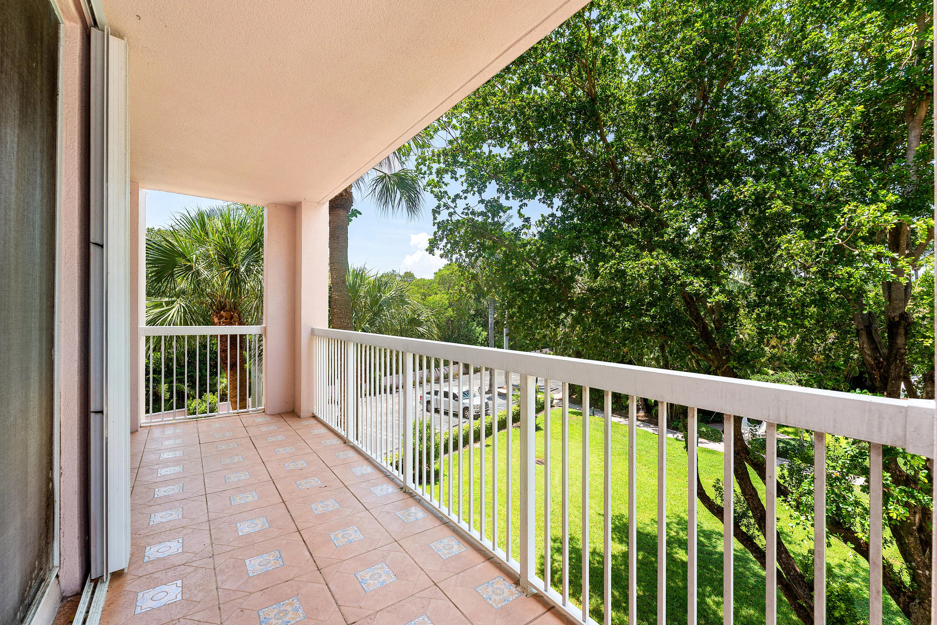 Private balcony with patterned tile flooring, white metal railings, and tropical foliage surroundings