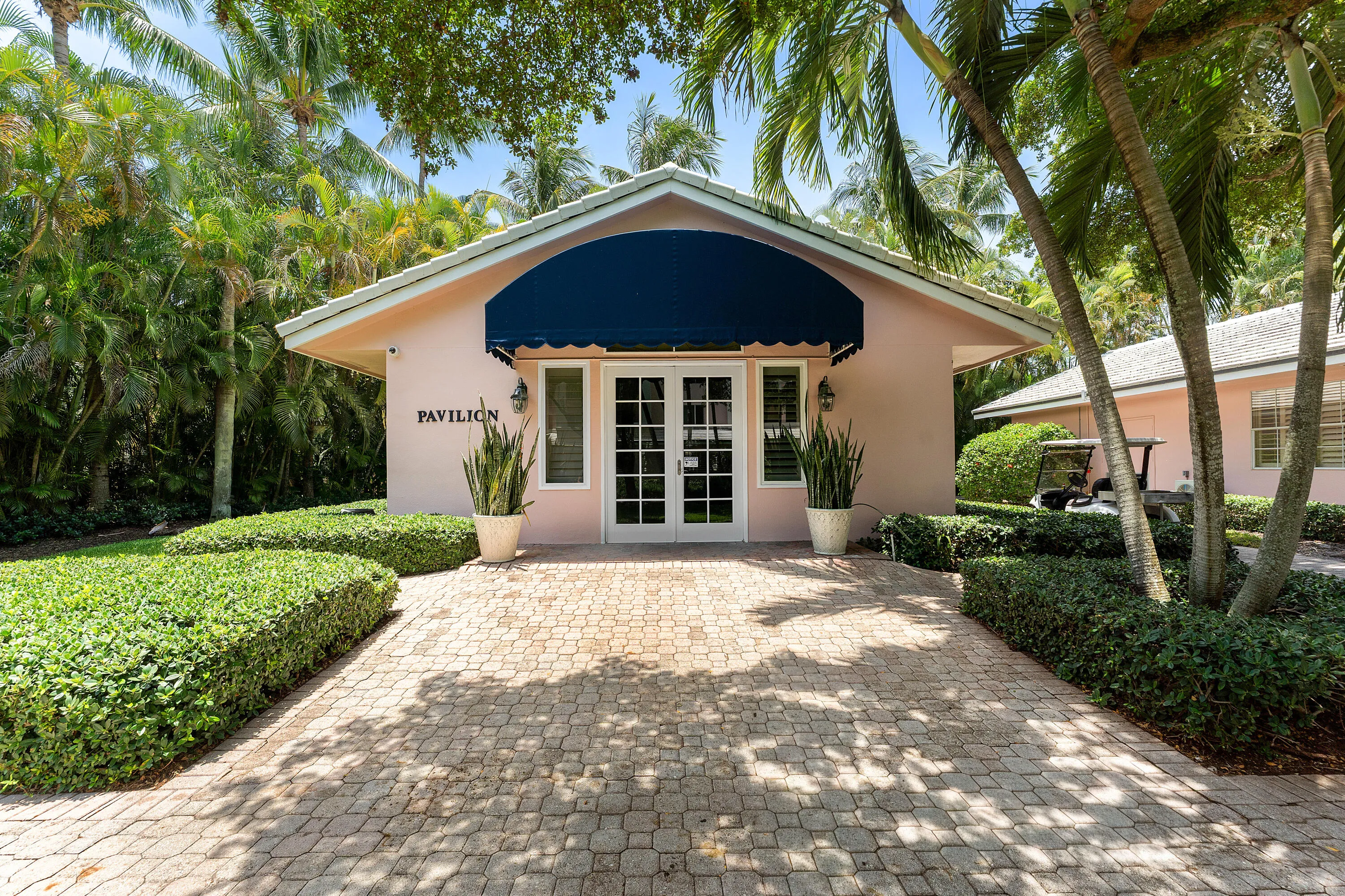 Pink stucco building with a blue awning, featuring white French doors and decorative exterior lighting