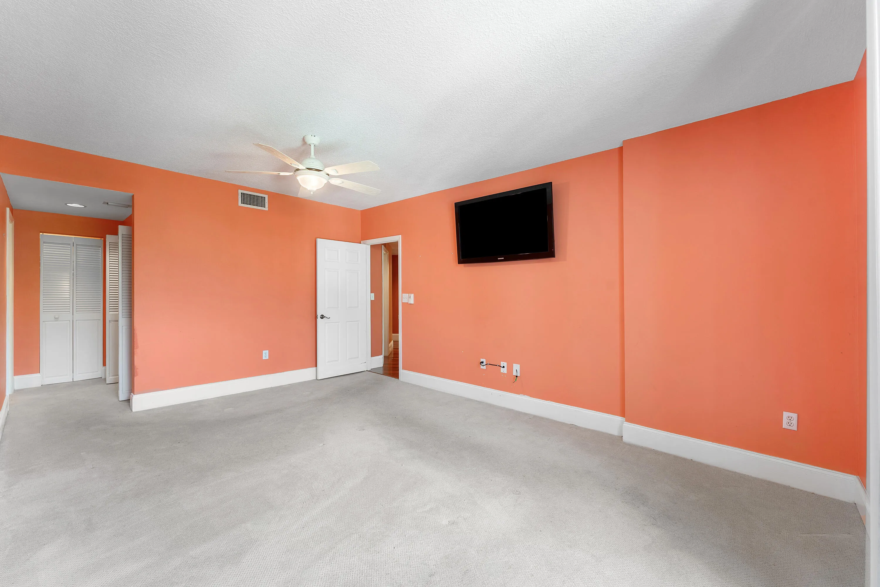 Spacious room with light-colored carpeting and vibrant orange walls