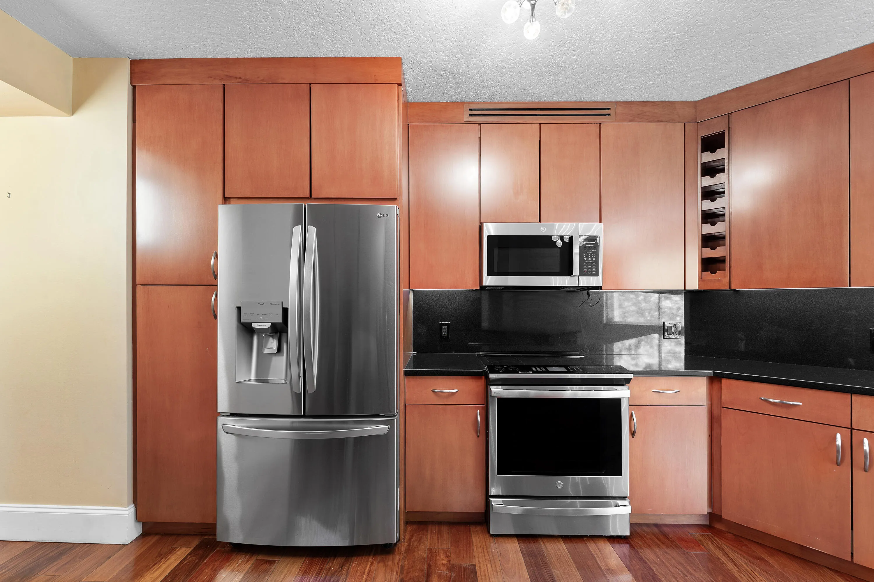 Kitchen featuring wood-finish flooring, full-height cabinetry, stainless steel appliances, dark countertops, and a built-in wine rack