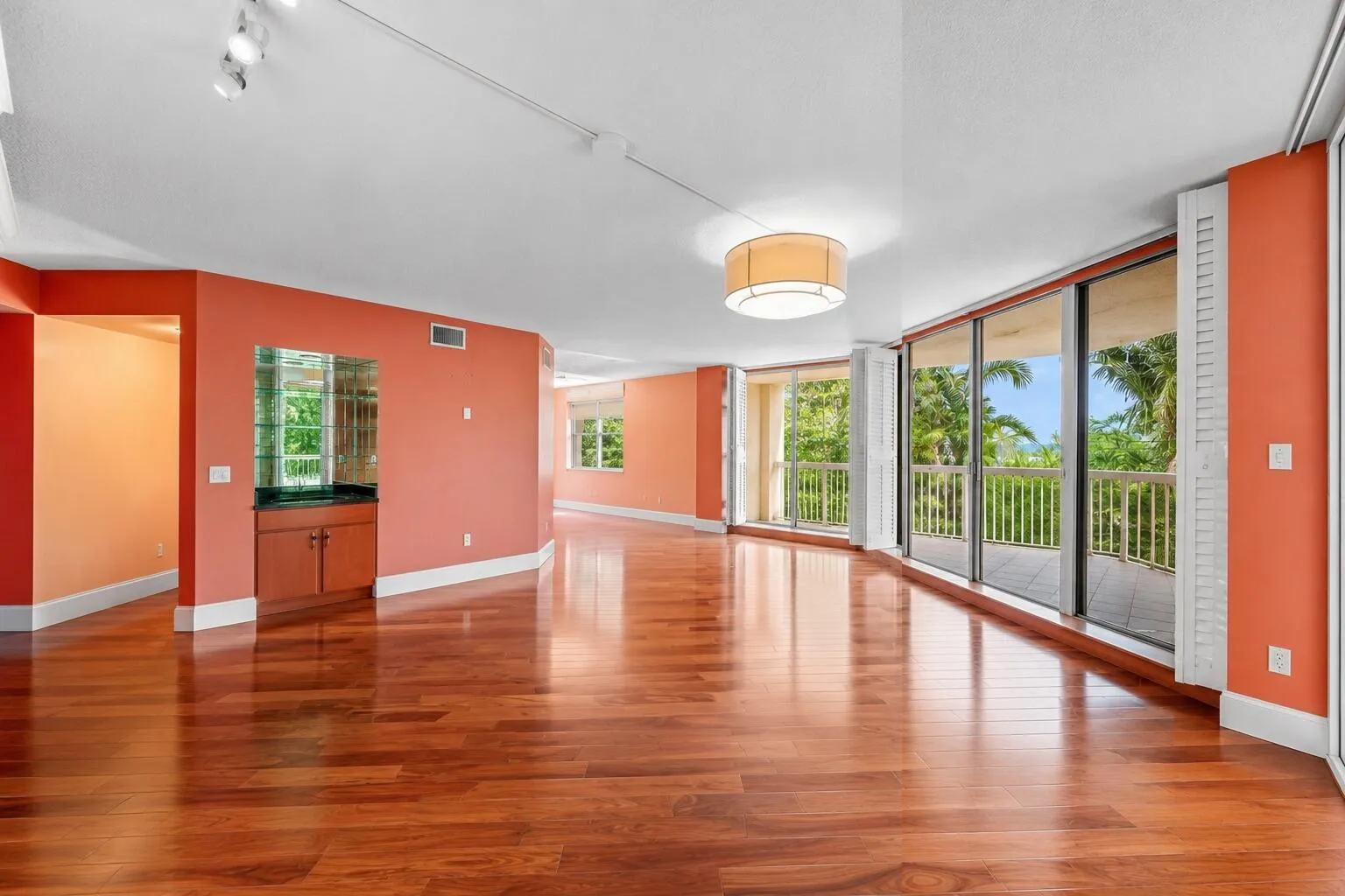Expansive interior featuring wood-finish flooring, a built-in wet bar with mirrored backsplash, and a series of floor-to-ceiling sliding glass doors opening to a balcony