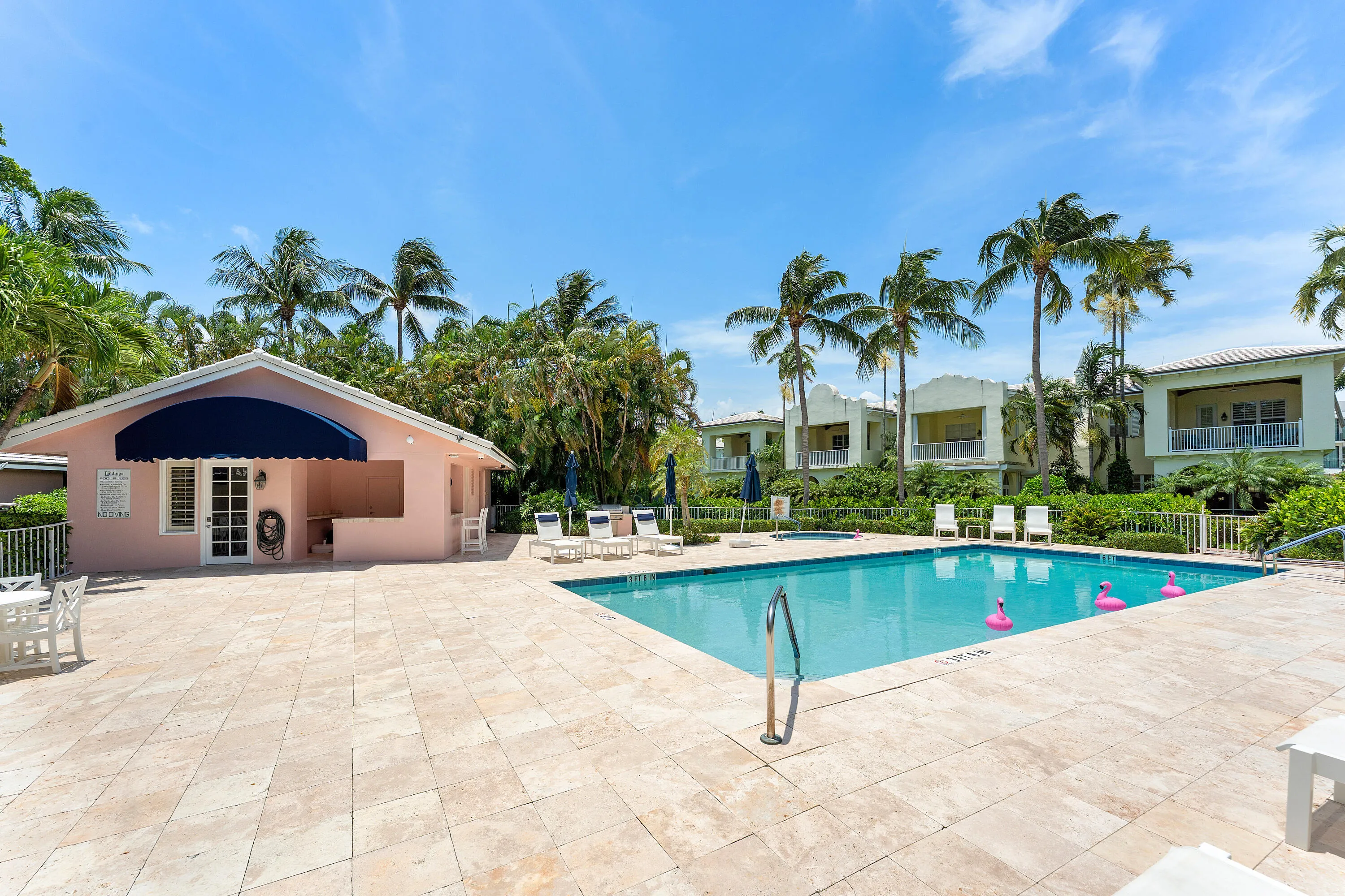 Expansive pool deck with light-toned paving stones, a rectangular swimming pool, and a poolside cabana featuring a blue awning