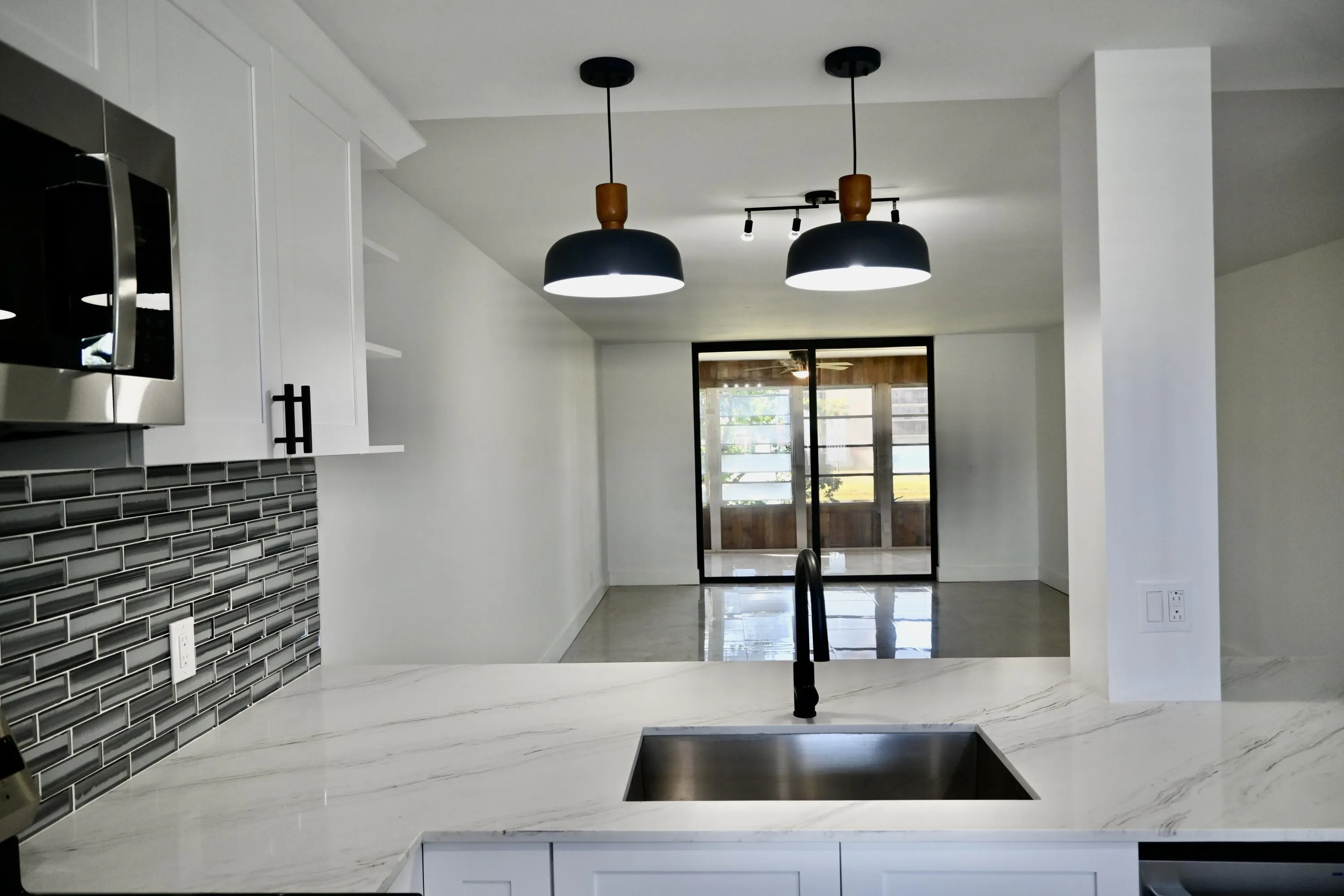 Kitchen featuring a stainless steel undermount sink with a matte black faucet, light-toned countertops, and a gray subway tile backsplash