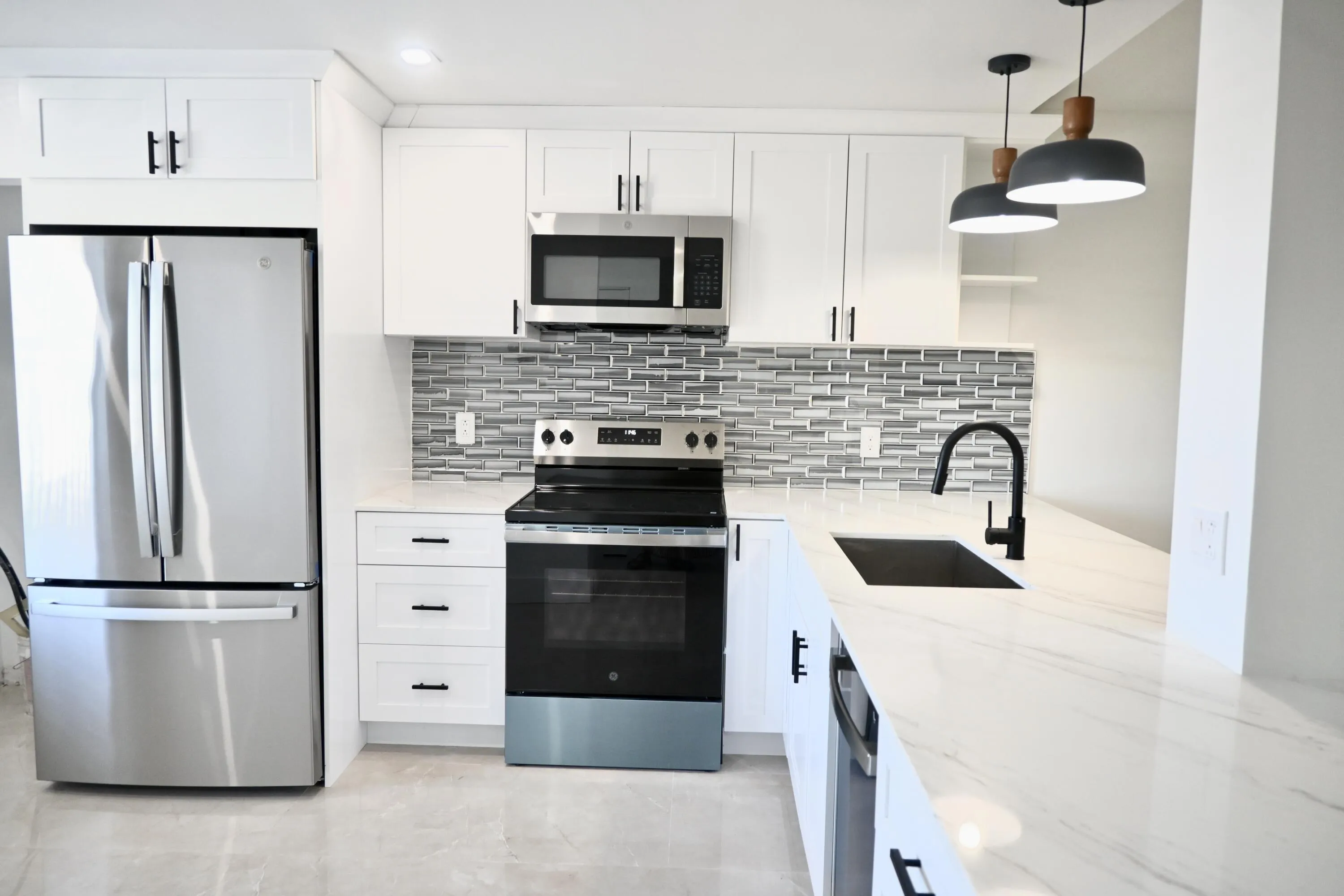 Kitchen featuring white shaker-style cabinetry, stainless steel appliances, a multi-tone tile backsplash, and light-colored countertops with veining