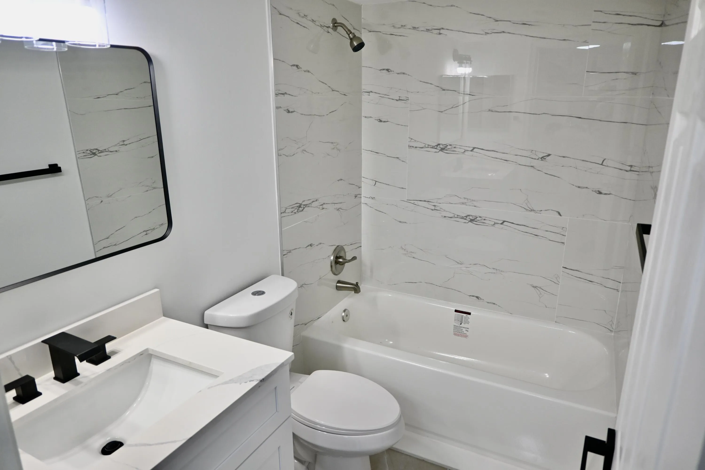 Bathroom featuring a white bathtub with a shower, a vanity with a white countertop and integrated sink, a contemporary black-framed mirror, and a modern black faucet