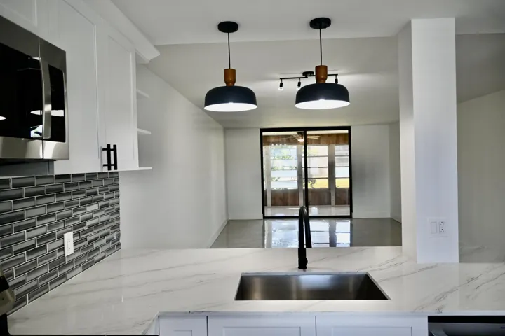 Kitchen featuring a stainless steel undermount sink with a matte black faucet, light-toned countertops, and a gray subway tile backsplash
