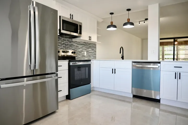 Modern kitchen featuring stainless steel appliances, white cabinetry with black hardware, a mosaic tile backsplash, and light-toned flooring