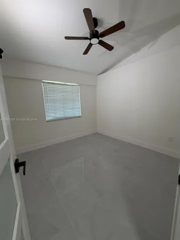 Light gray tile flooring with a subtle pattern, white walls, and a dark-toned ceiling fan
