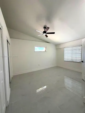Vaulted ceiling with a ceiling fan, light gray tile flooring, and two distinct window placements with blinds