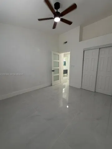 Polished tile flooring, ceiling fan, white walls, and white sliding closet doors