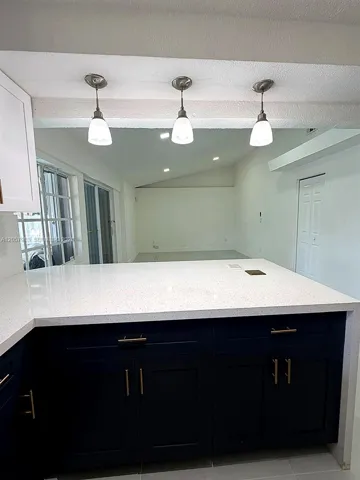 Kitchen island featuring a white speckled countertop, dark blue cabinetry, and gold-finish hardware