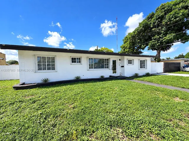 White stucco exterior with a dark fascia, multiple pane windows, a white privacy fence, and a concrete pathway