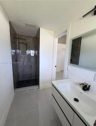 Glass-enclosed shower with dark-toned tile surround, light gray tile flooring, and a floating vanity with an integrated sink