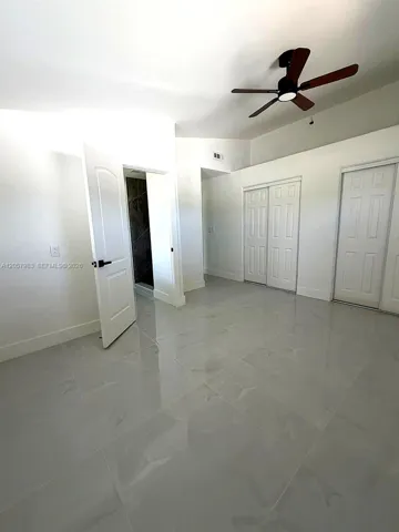 Spacious room featuring light-toned tile flooring, a dark-toned ceiling fan, and white doors with dark hardware