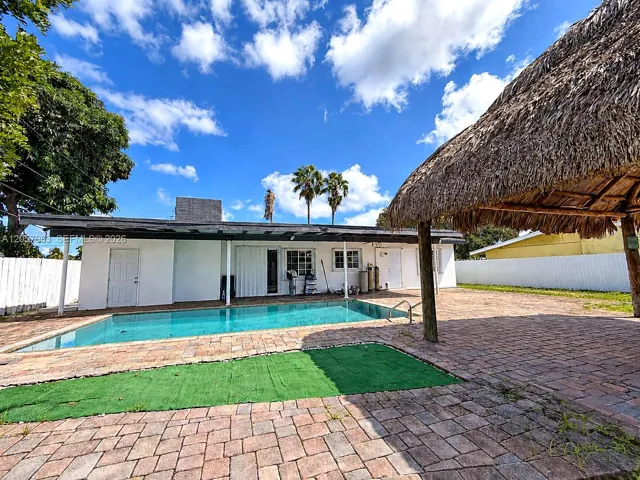Swimming pool with paver decking, adjacent to a thatched-roof structure