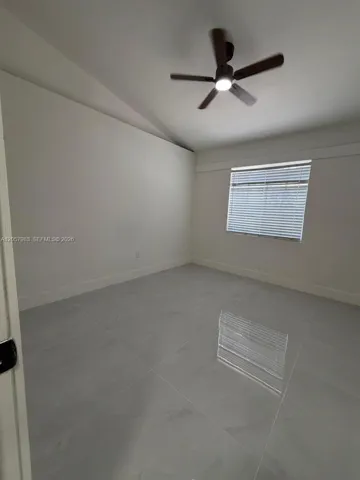 Vaulted ceiling, ceiling fan with integrated lighting, large format tile flooring, window with horizontal blinds, and white baseboards