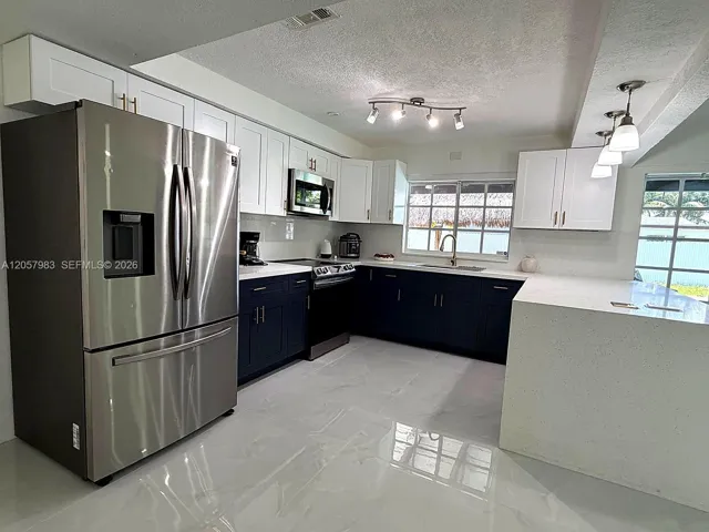 Modern kitchen with glossy tile flooring, stainless steel appliances, two-tone cabinetry, and light-colored countertops