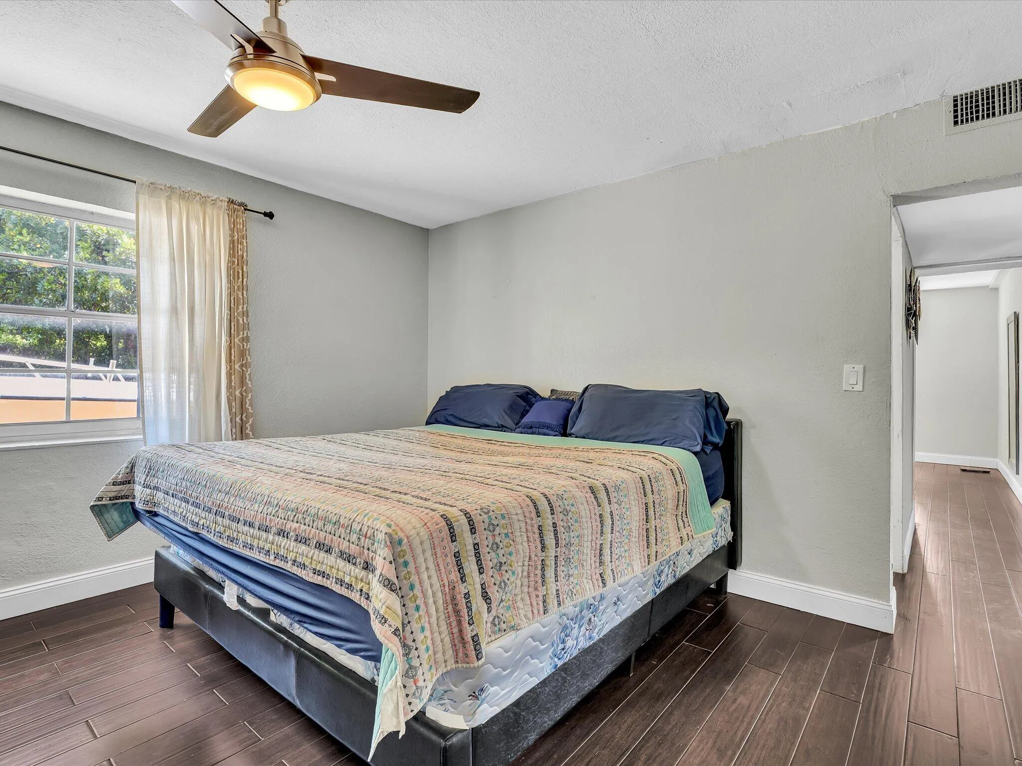 Room featuring wood-finish flooring, a ceiling fan with integrated lighting, a window with a curtain rod, and a white baseboard trim