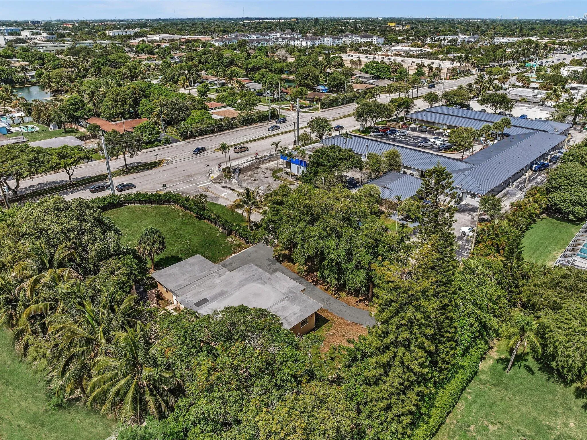 Aerial perspective showcasing a property surrounded by mature trees, a manicured lawn area, and a paved driveway