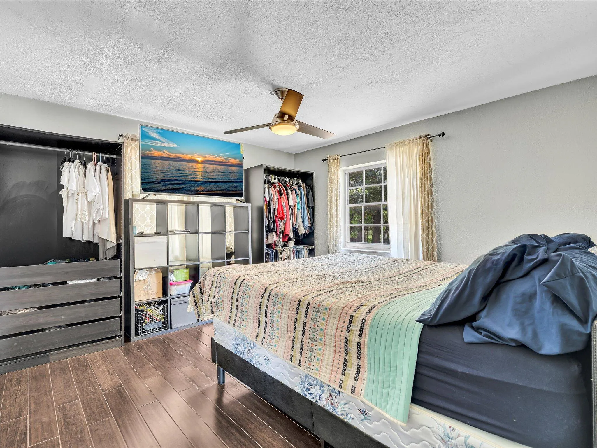 Spacious room featuring wood-finish flooring, a multi-pane window, and a ceiling fan with integrated lighting