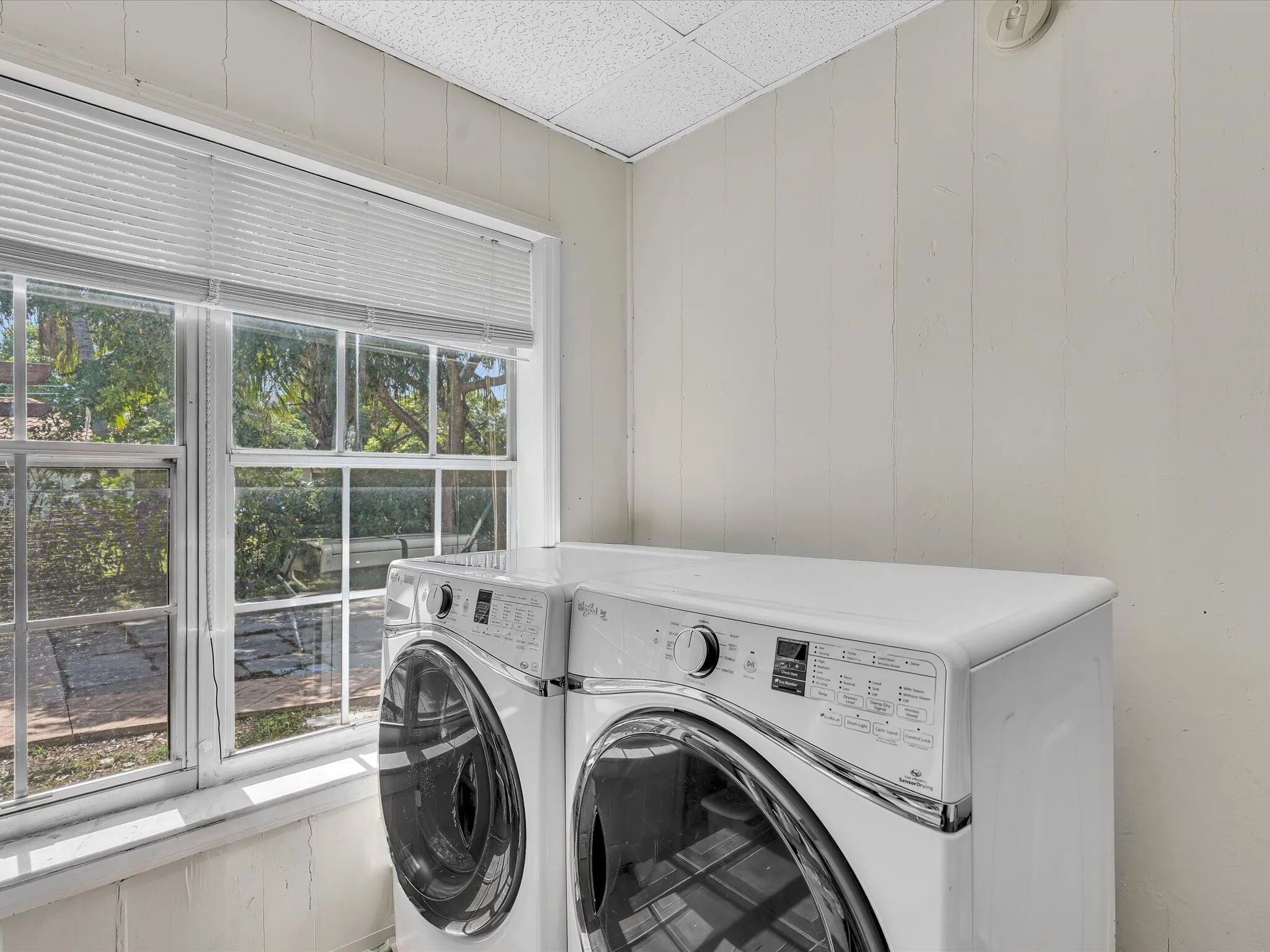 Laundry area featuring a large window, paneling walls, and a textured ceiling