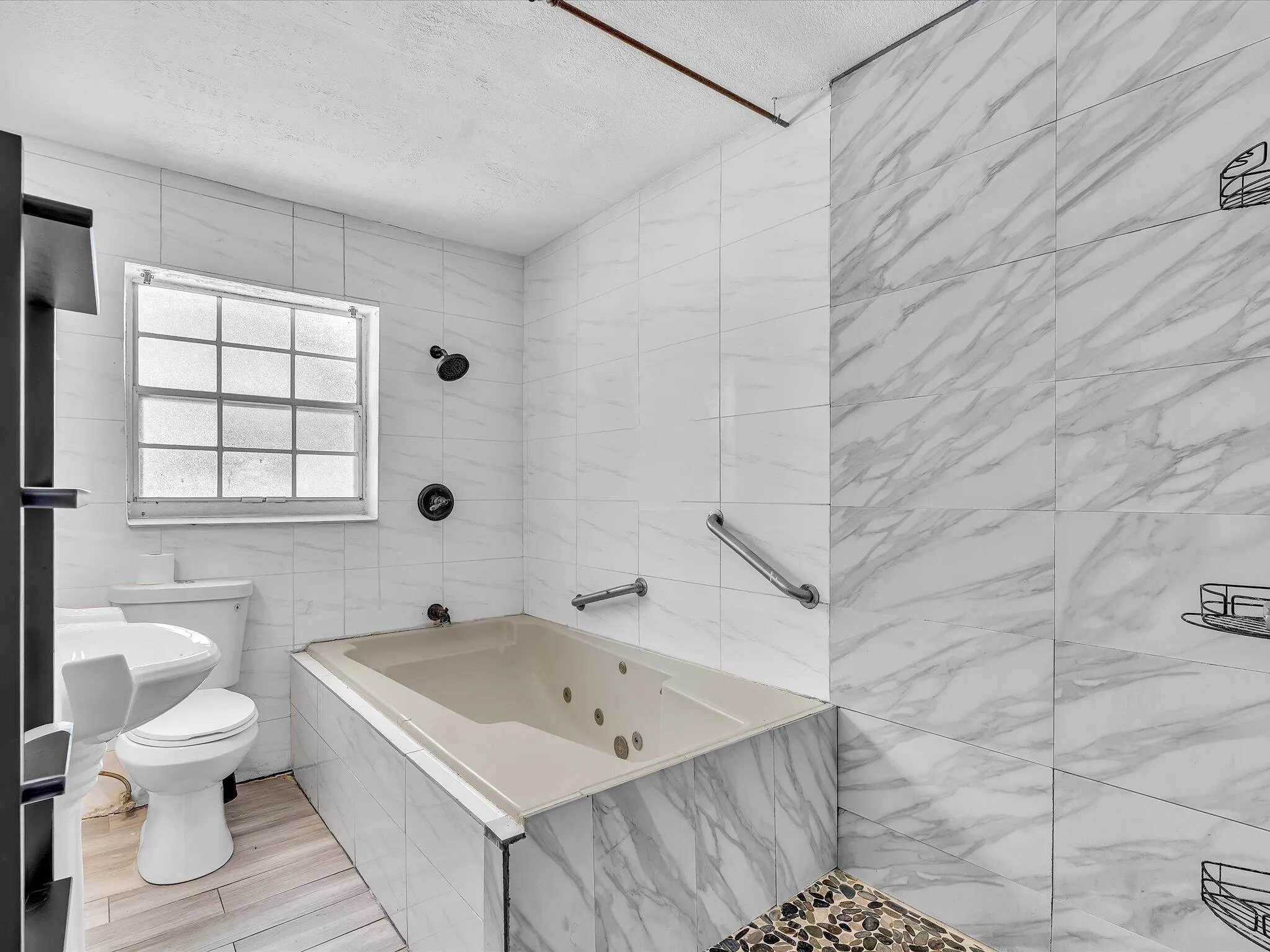 Bathroom featuring a jetted tub, a separate shower with a pebble floor, and white and gray marbled wall tiling