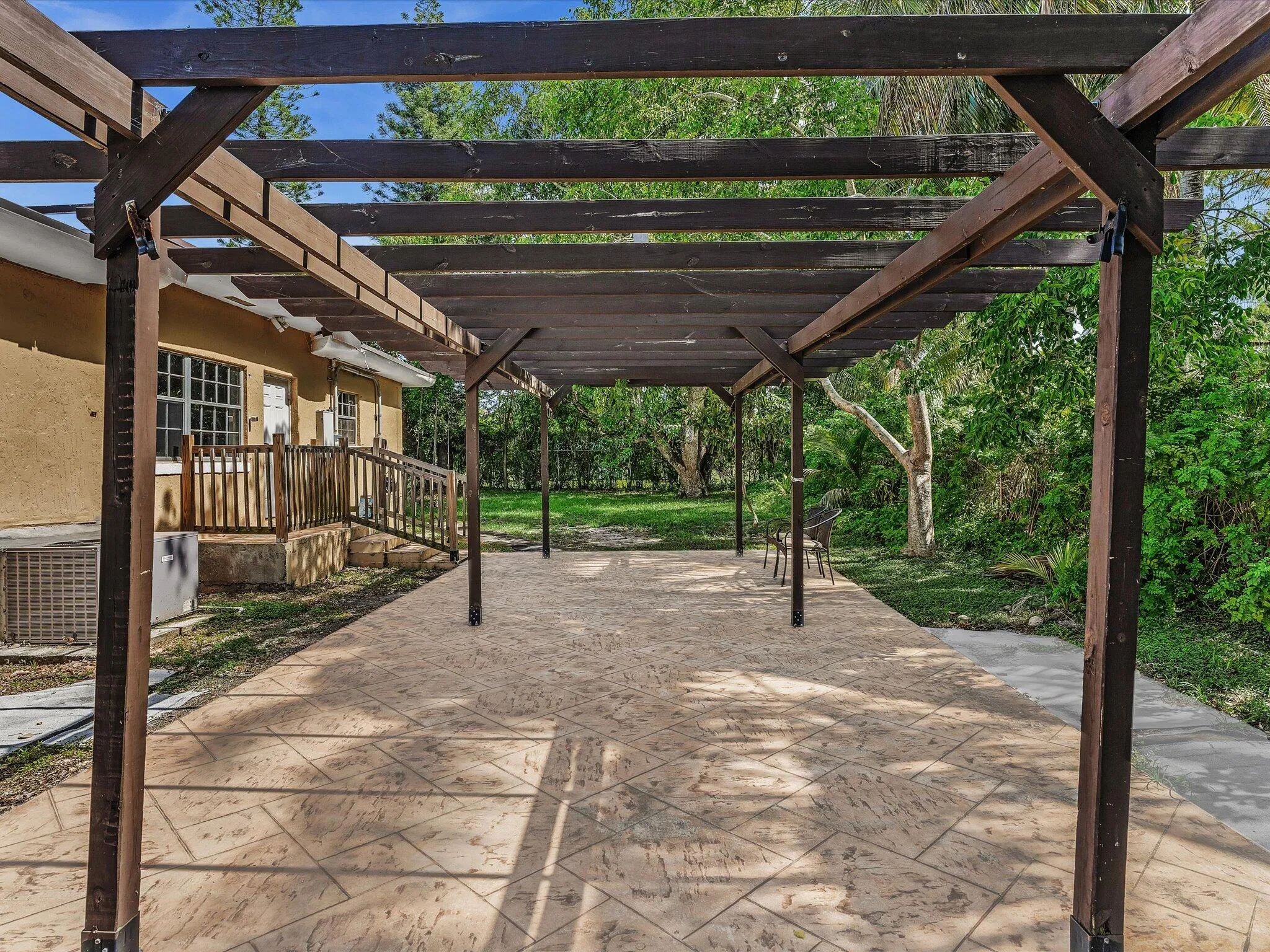 Expansive covered patio featuring a dark wood pergola, stamped concrete flooring, and direct access to an exterior wooden staircase