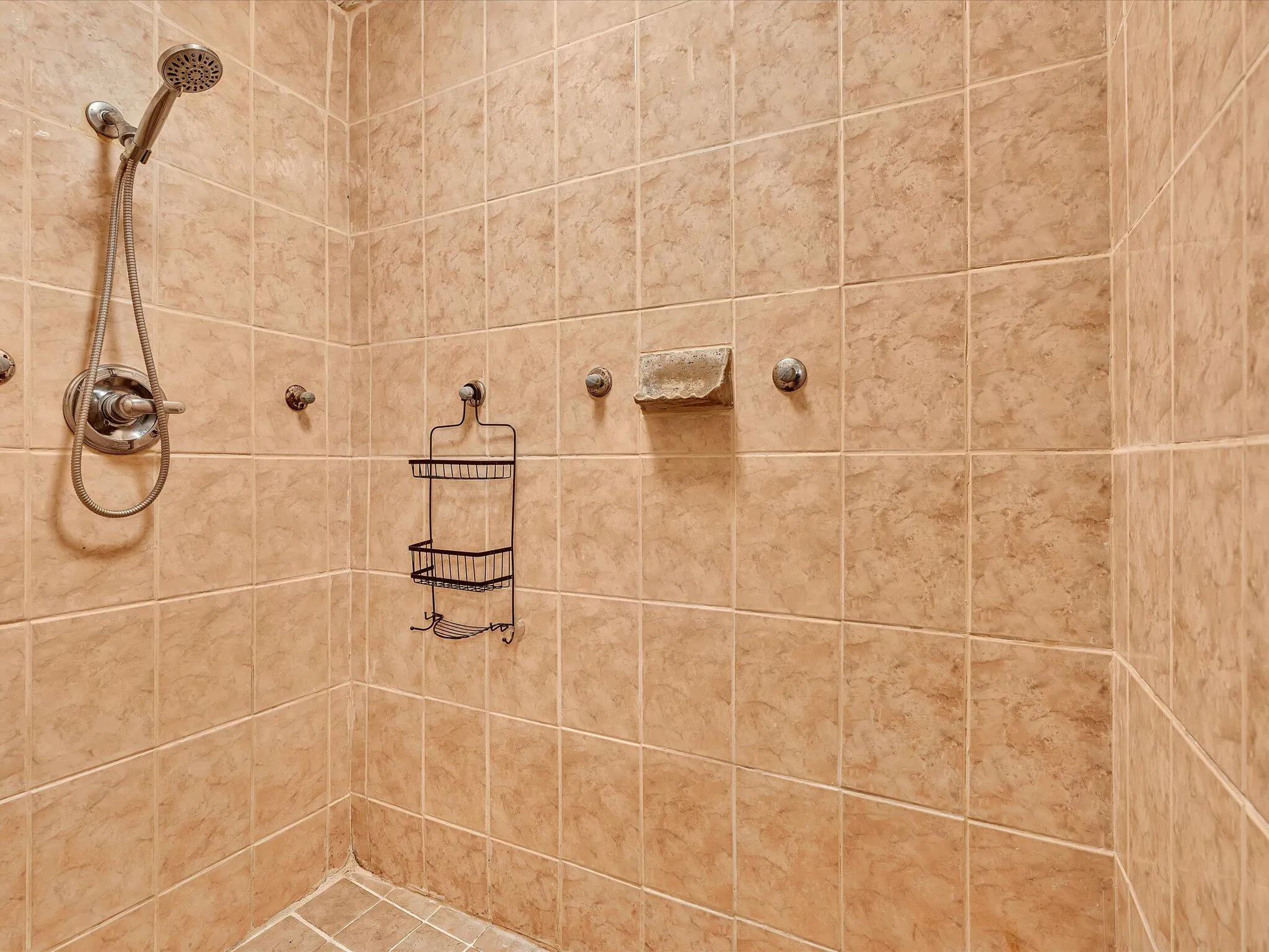 Shower enclosure featuring full-height tiled walls and floor, a handheld shower fixture, and a built-in soap dish
