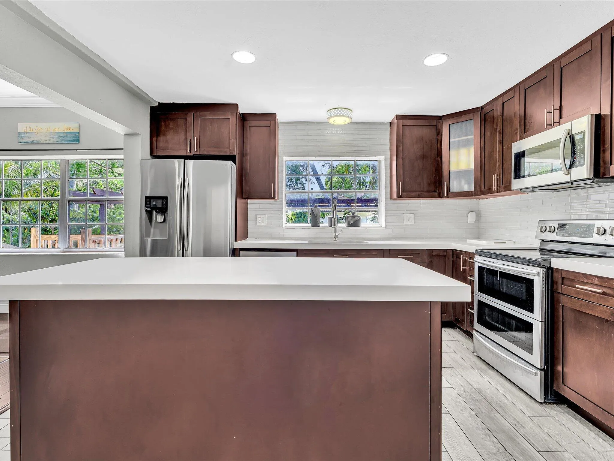 Kitchen featuring a central island with a solid surface countertop, rich wood-finish cabinetry, stainless steel appliances, white subway tile backsplash, and light wood-finish flooring