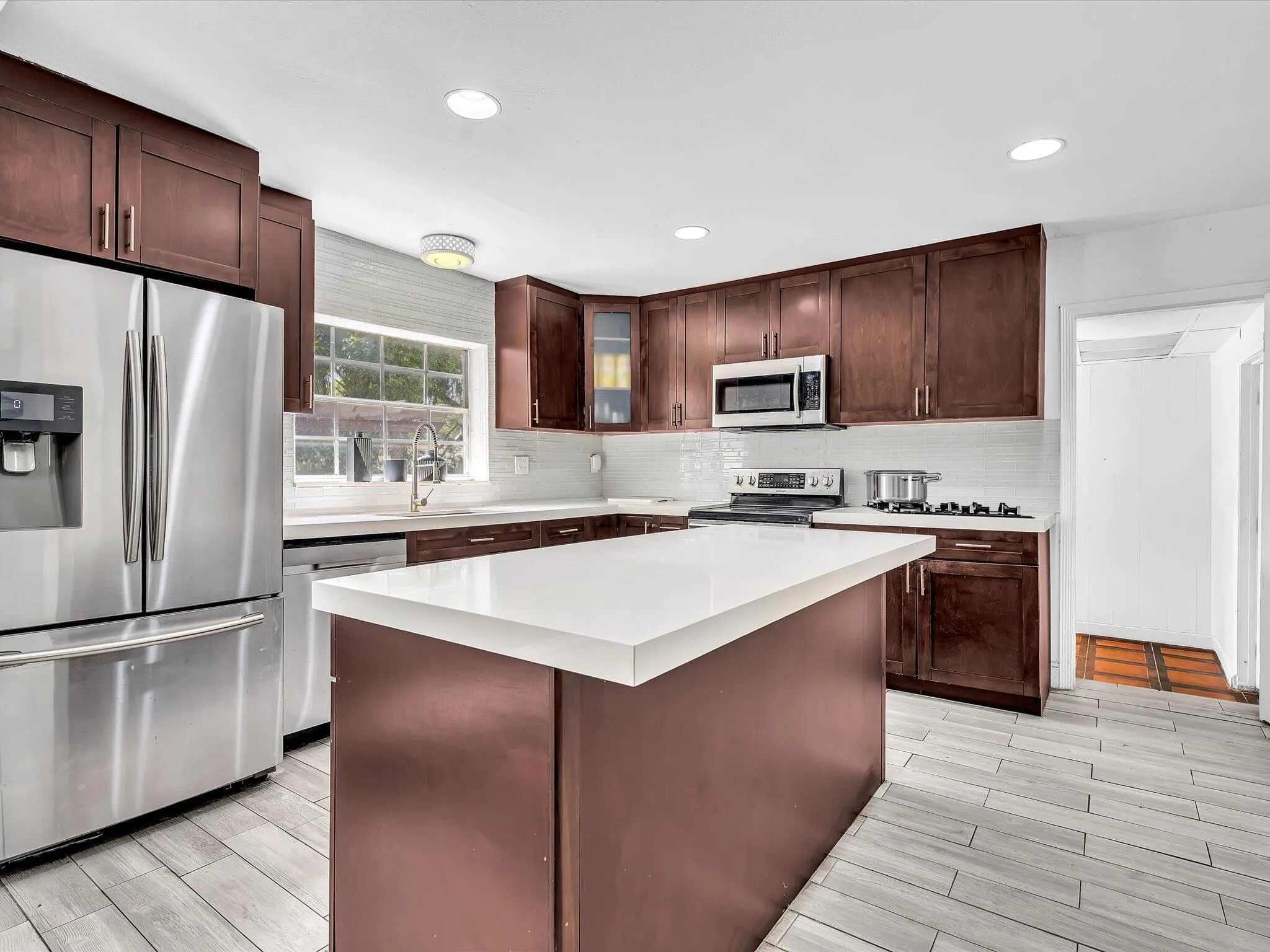 Kitchen featuring an island with a white countertop, dark wood-finish cabinetry, stainless steel appliances, and wood-finish flooring