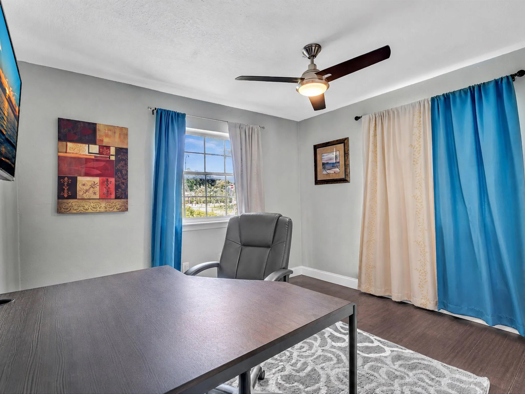 Bright room featuring a window with exterior views, dark wood-finish flooring, and a ceiling fan with integrated lighting