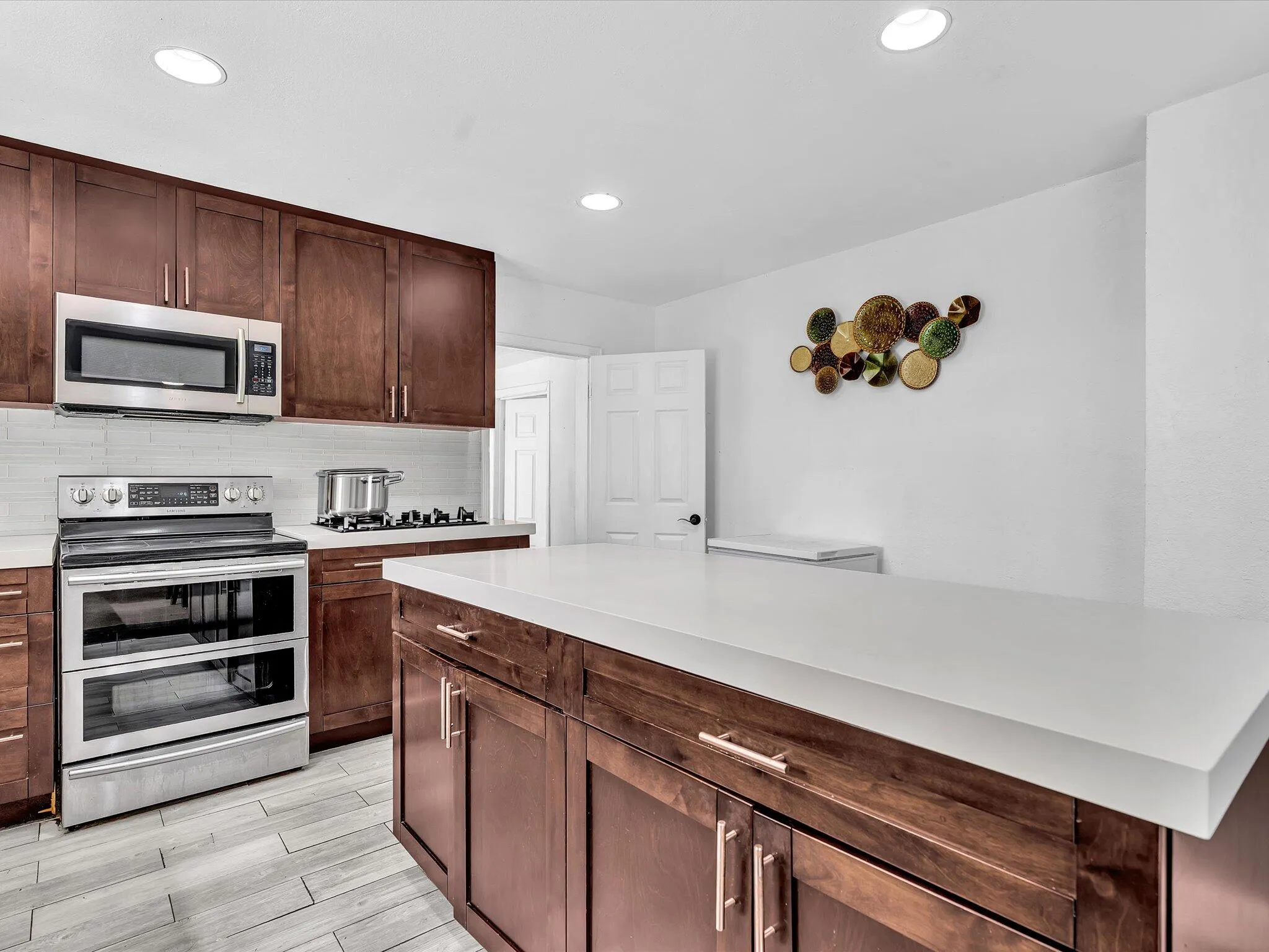 Kitchen featuring a central island with a light-toned countertop, wood-finish cabinetry, stainless steel appliances, and wood-look flooring