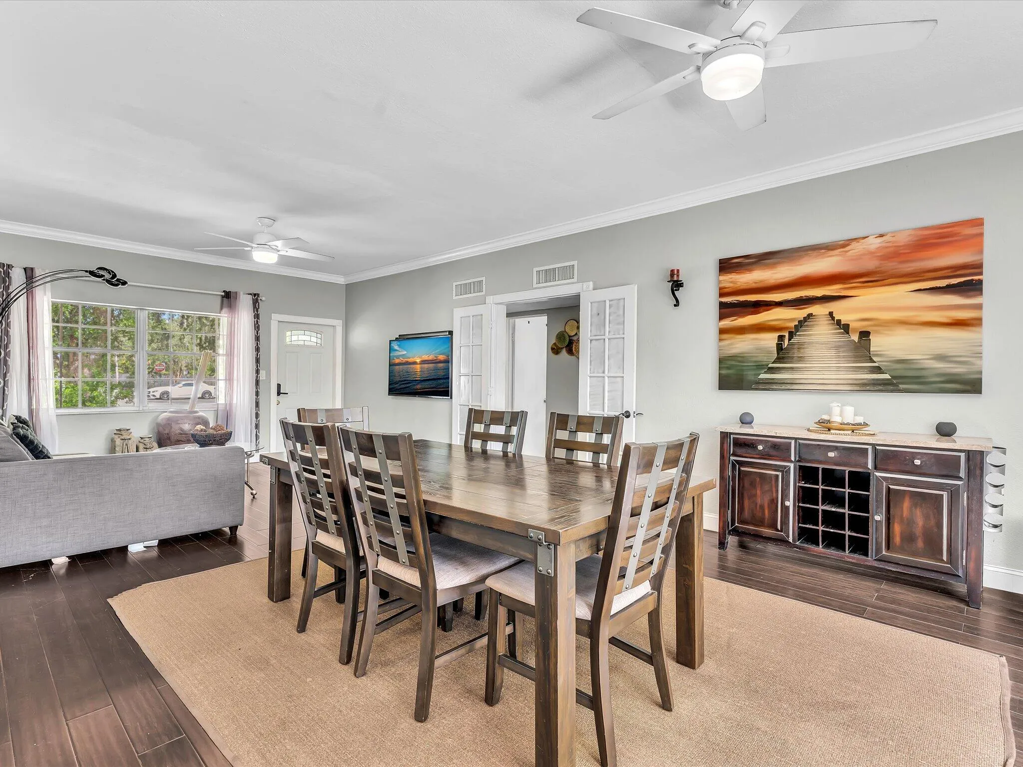 Open-concept living and dining area featuring wood-finish flooring, two ceiling fans, and a white paneled front door with a decorative glass insert