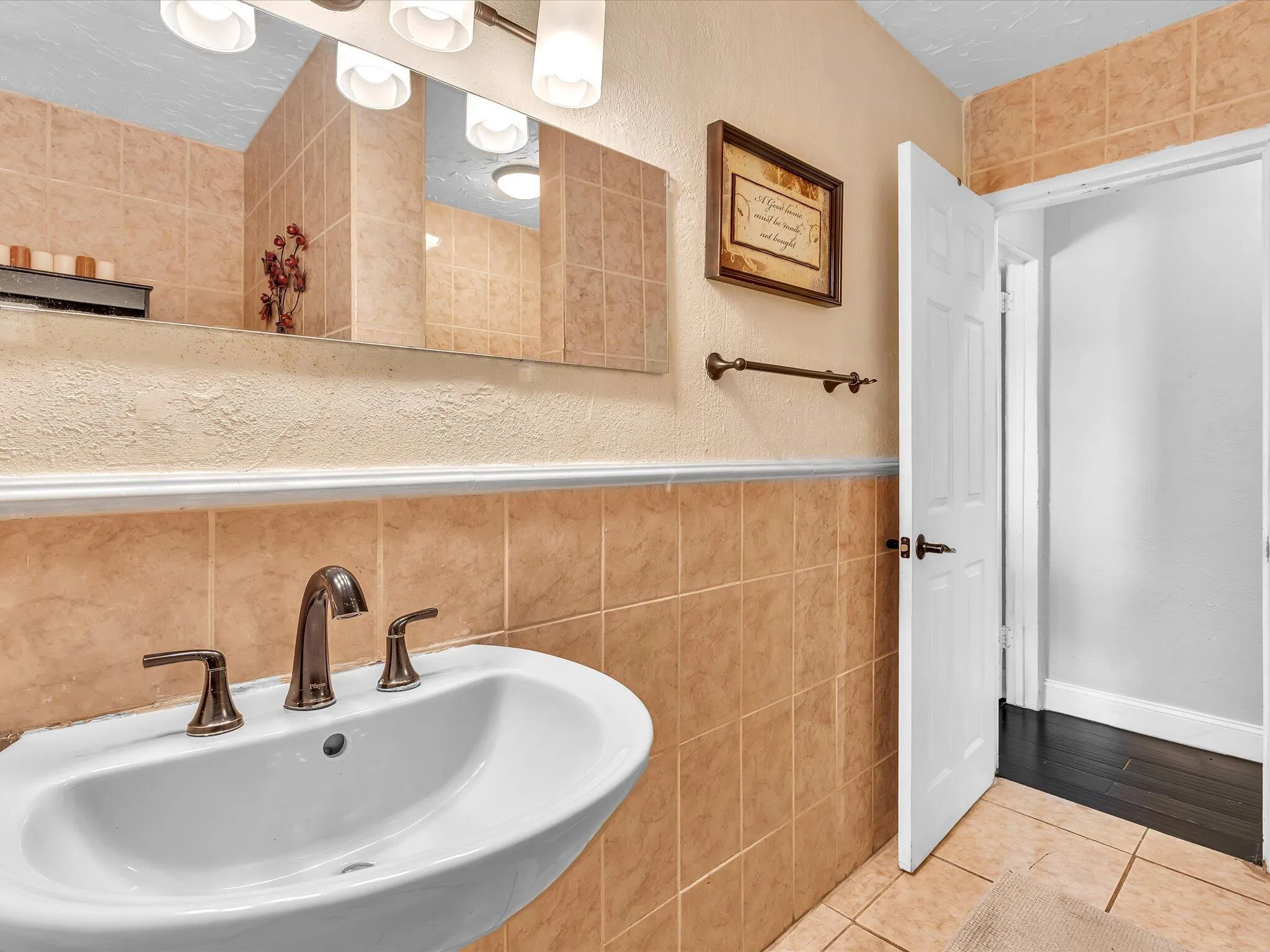 Pedestal sink with bronze-finish faucet, illuminated by a four-bulb vanity light fixture