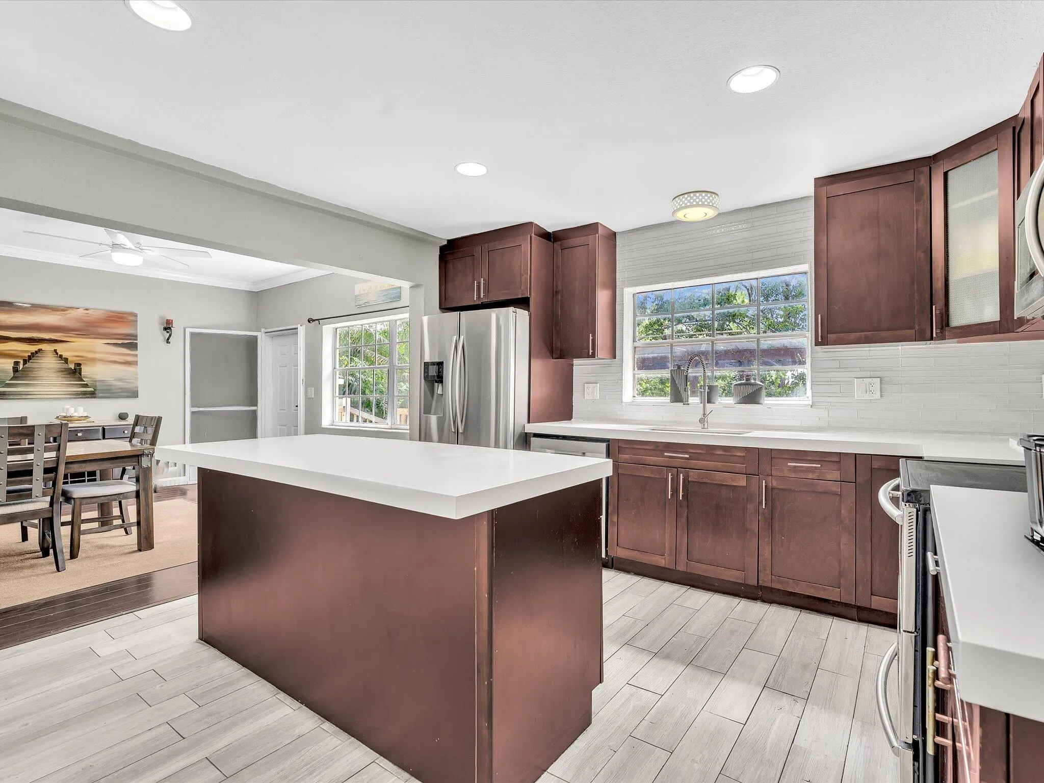 Contemporary kitchen featuring a center island with a white countertop, recessed lighting, wood-finish cabinetry, stainless steel appliances, and tile flooring