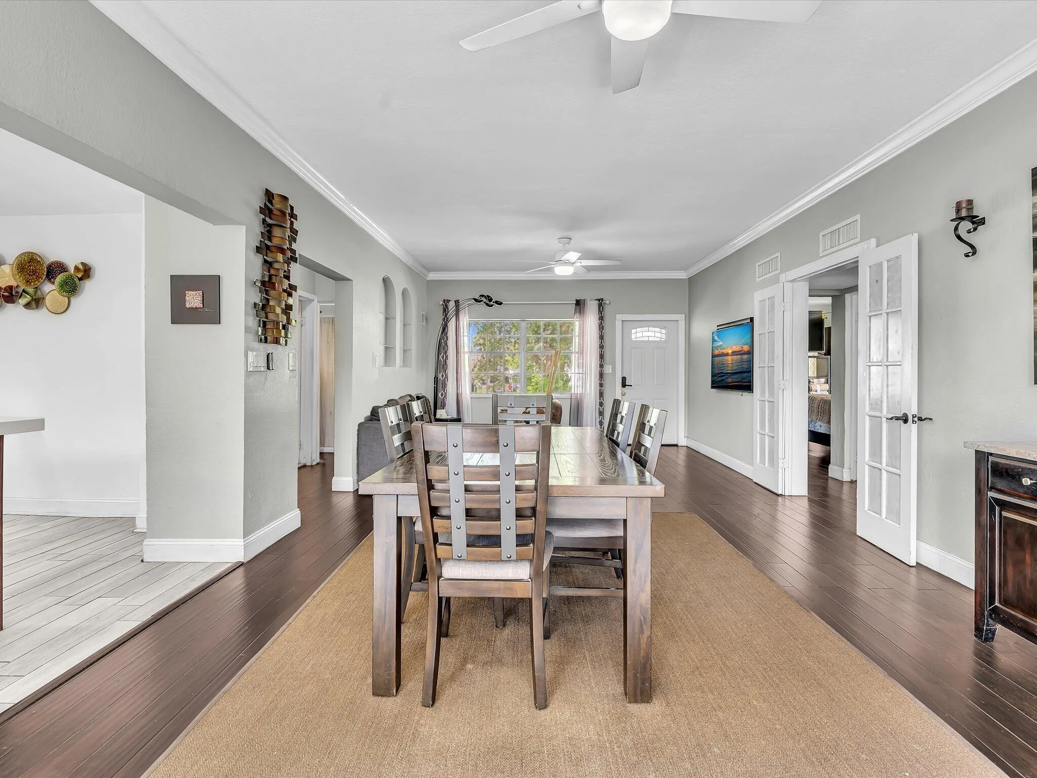 Open-concept dining area featuring dark wood-finish flooring, white crown molding, and a ceiling fan with integrated lighting
