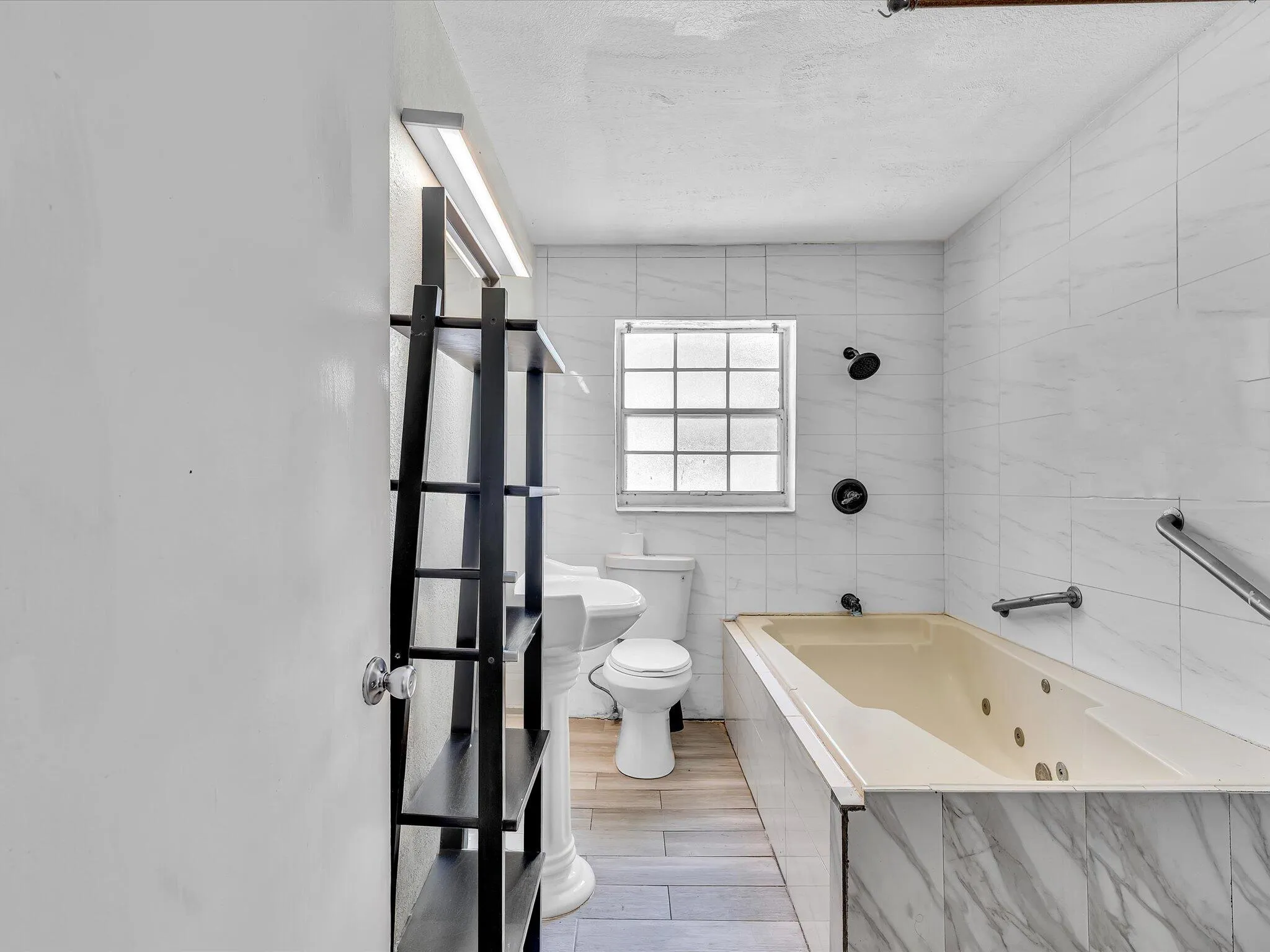 Bathroom featuring a jetted tub with marble-look tile surround, pedestal sink, and tiled shower area