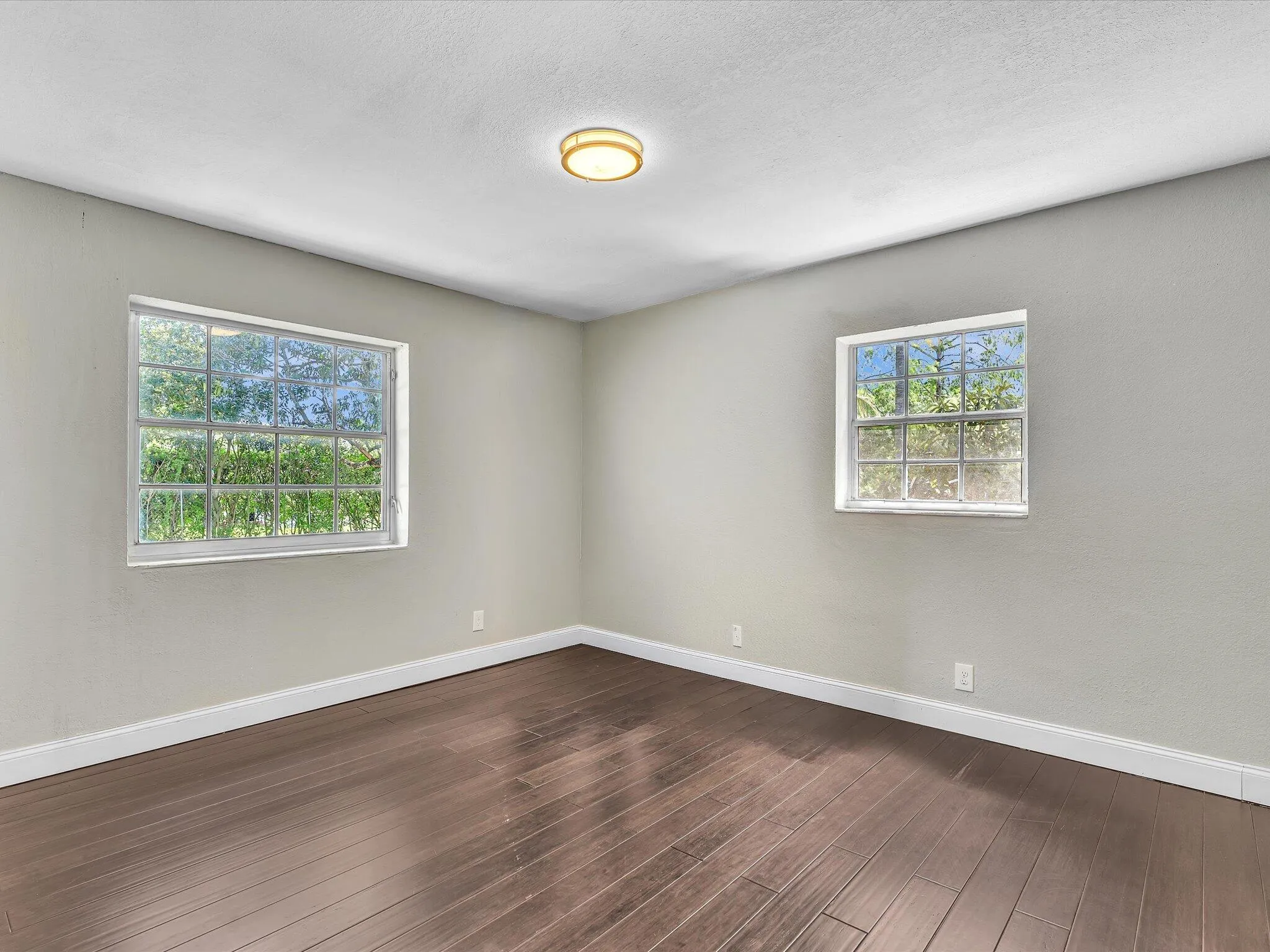Spacious room featuring rich wood-finish flooring, light gray walls, white baseboards, and a contemporary ceiling light fixture