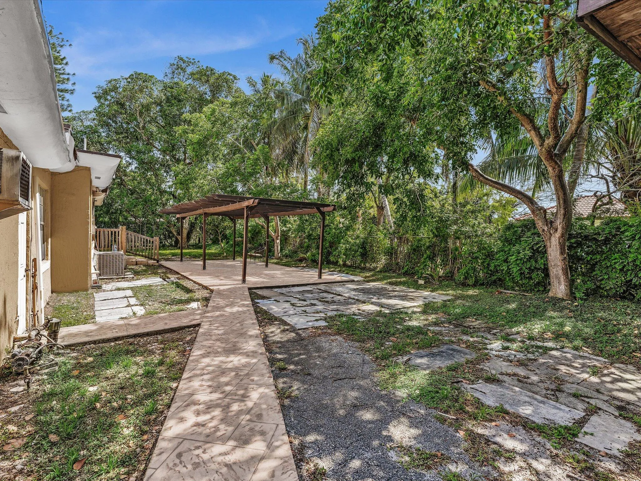 Expansive outdoor area featuring a pergola-covered patio, concrete pathways, and lush mature trees