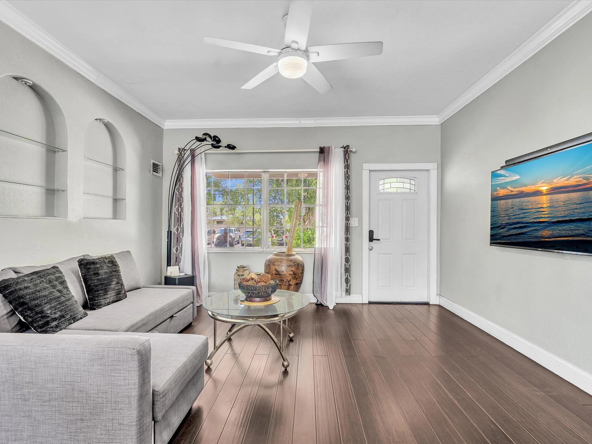 Spacious living area featuring wood-finish flooring, a ceiling fan with integrated lighting, and two recessed arched display niches
