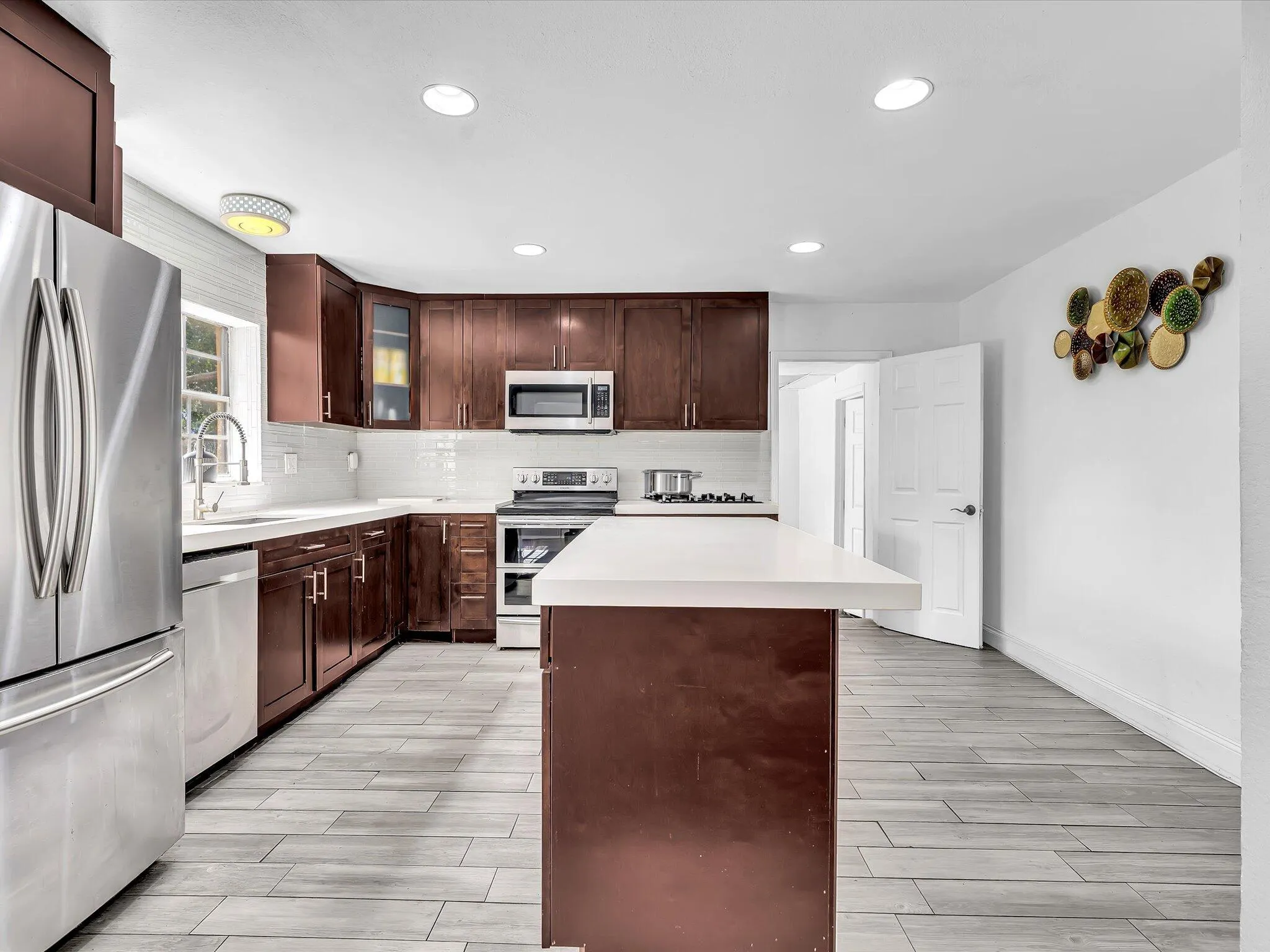 Kitchen featuring dark wood cabinetry, stainless steel appliances, white subway tile backsplash, light-toned countertops, and wood-finish flooring