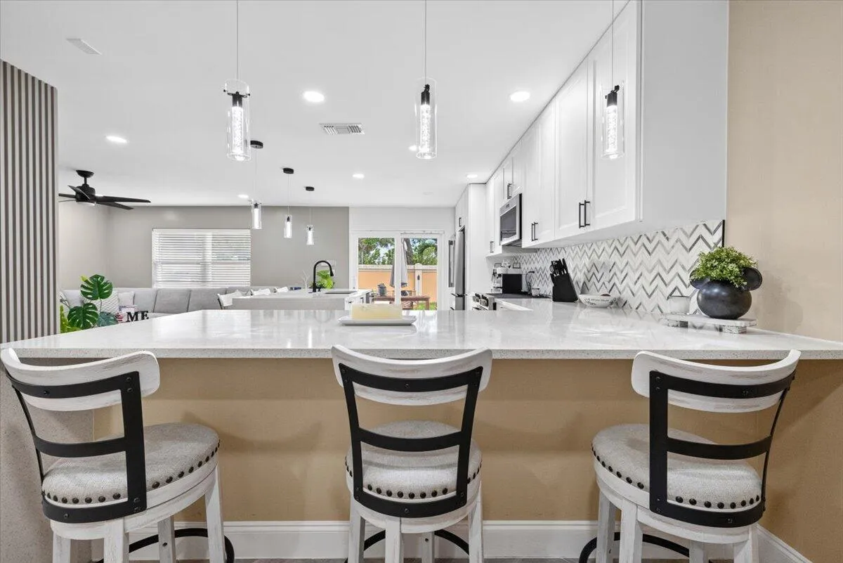 Kitchen island featuring a light-colored countertop, white shaker-style cabinetry, a chevron-patterned backsplash, and pendant lighting fixtures