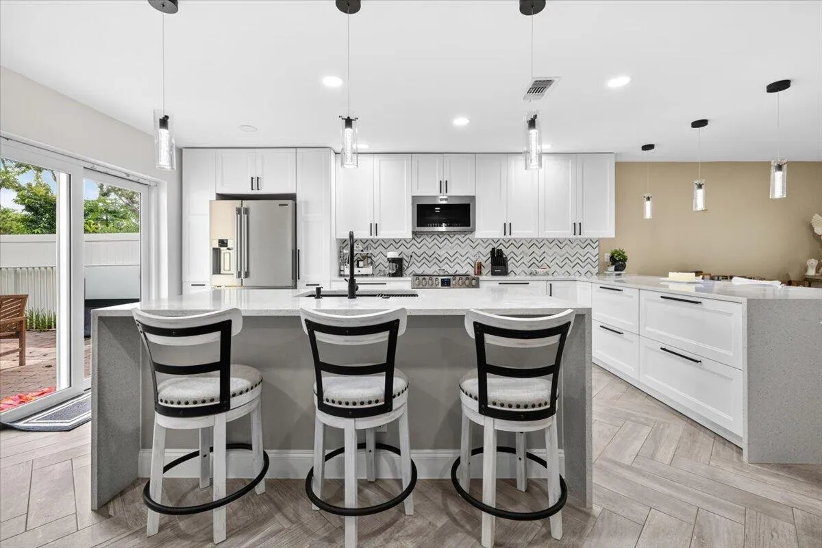 Open-concept kitchen featuring an expansive island with seating, stainless steel appliances, white cabinetry, and chevron-patterned backsplash