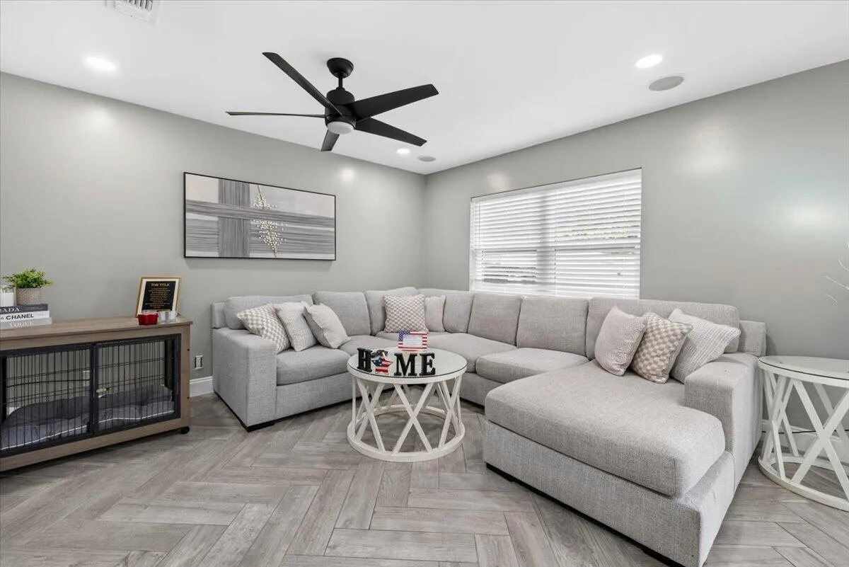 Living space featuring herringbone-patterned wood-finish flooring, recessed lighting, and a modern black ceiling fan