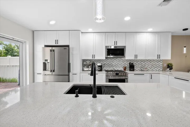 Expansive kitchen island featuring a black undermount sink with integrated drying rack, quartz countertop, and black matte faucet