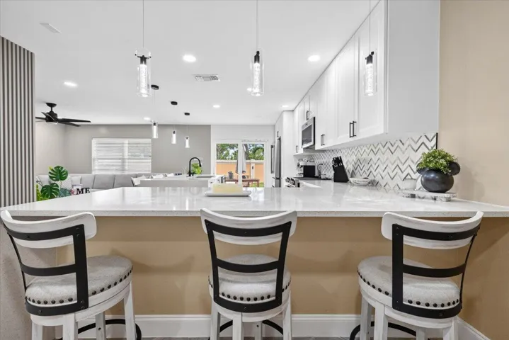 Kitchen island featuring a light-colored countertop, white shaker-style cabinetry, a chevron-patterned backsplash, and pendant lighting fixtures