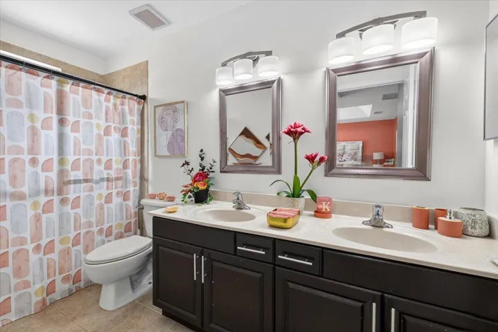 Double vanity with dark wood cabinetry, light-toned countertop, and dual framed mirrors with overhead lighting
