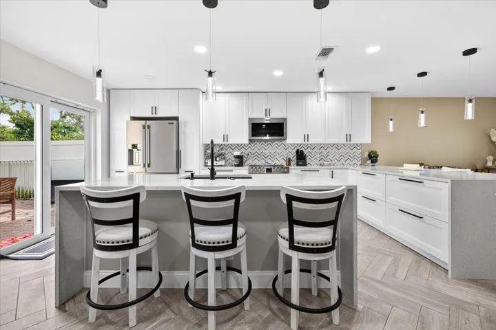 Open-concept kitchen featuring an expansive island with seating, stainless steel appliances, white cabinetry, and chevron-patterned backsplash